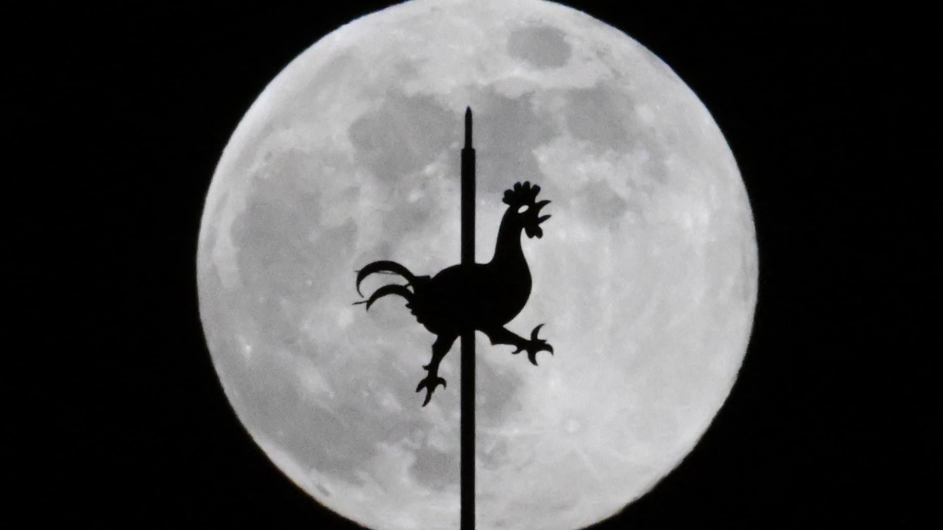 La girouette de l'église Saint-Pierre est photographiée devant la première pleine lune de l'année, la « Lune du Loup », dans le village bavarois de Hoehenkirchen-Siegertsbrunn, dans le sud de l'Allemagne, le 13 janvier 2025.