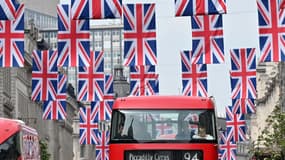 Des bus rouges passent sous les drapeaux du Royaume-Uni dans le centre de Londres, le 30 avril 2023 avant la cérémonie de couronnement de Charles III 