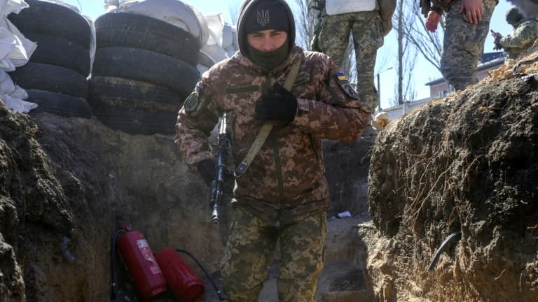 Un soldat ukrainien court se mettre à l'abri dans une tranchée  alors qu'un avion russe survole la zone située à côté d'une caserne touchée la veille par des roquettes russes,  à Mykolaïv, dans le sud de l'Ukraine, le 19 mars 2022.