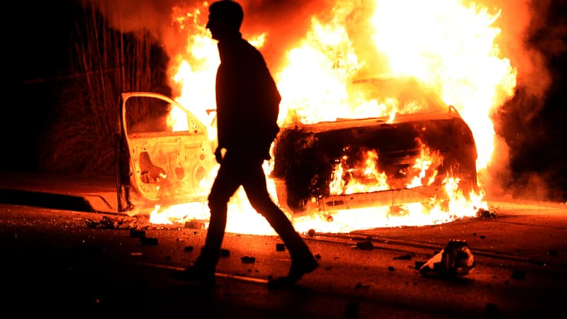 Un manifestant passe devant une voiture brûlée à Ferguson, dans la nuit de lundi à mardi.