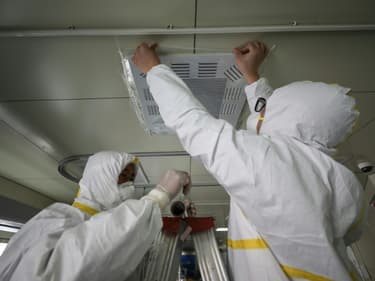 Des employés d'un hôpital de Wuhan scellent une bouche d'aération d'une unité d'isolement le 12 mars 2020, avant la réouverture aux patients non-Covid-19