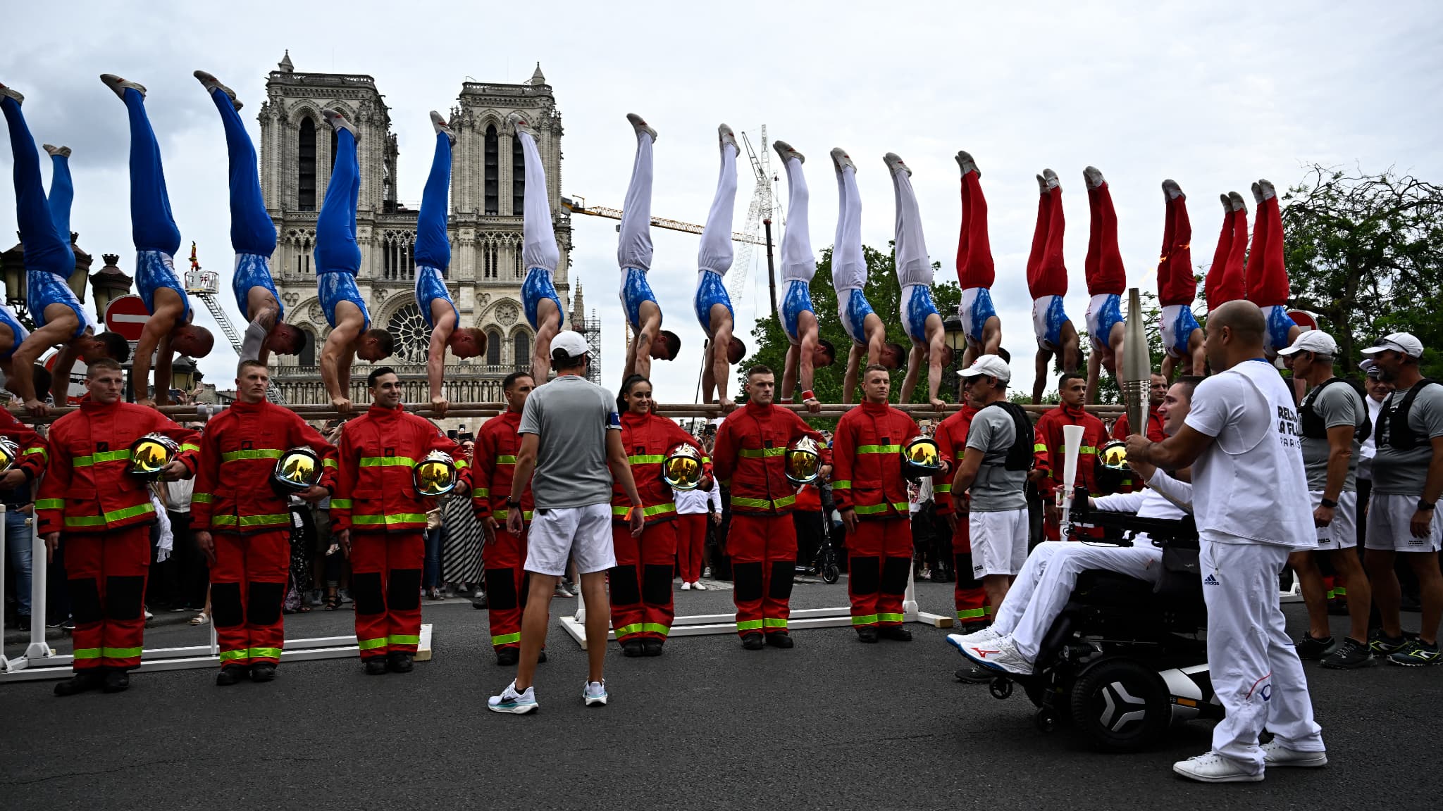 Le relais de la flamme olympique devant des pompiers de Paris près de la cathédrale Notre-Dame le dimanche 14 juillet 2024.