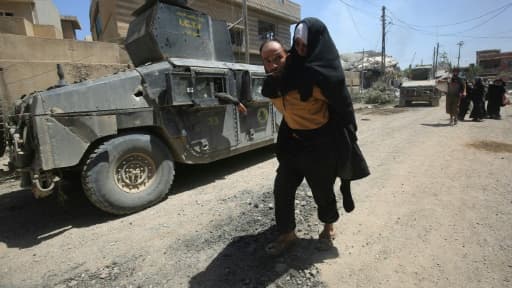 Un homme porte une femme sur son dos alors qu'ils fuient les combats entre les forces irakiennes et les jihadistes de l'EI, le 17 mai 2017 à Mossoul-Ouest