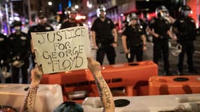Un manifestant portant une affiche "Justice pour George Floyd" devant des policiers à New York ce dimanche 31 mai 2020.