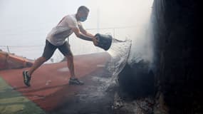 Un habitant tente d'éteindre un incendie près d'un mur lors d'un incendie de forêt qui se propage dans le quartier de l'Estaque à Marseille, dans le sud de la France, le 8 juillet 2025.