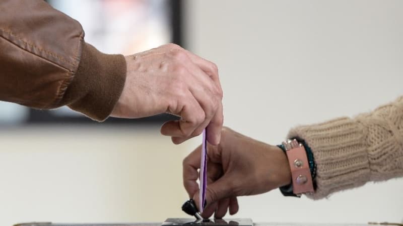Une personne en train de mettre son bulletin dans une urne.