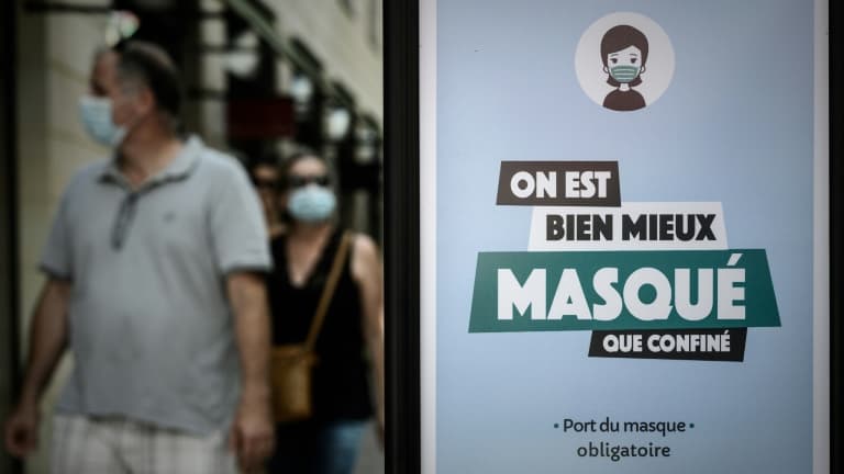 Un homme et une femme masqués passe devant une panneau d'information sur le port obligatoire du masque.