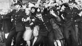 Des fans des Beatles sont contenus par la police devant les grilles du Palais de Buckingham, lors d'une apparition publique du groupe, reçu par la reine, le 26 octobre 1965 à Londres.