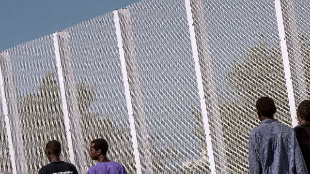Des migrants marchent à côté d'une clôture bordant la Jungle, à Calais, le 8 septembre 2016.