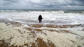 Une personne présente sur une la plage de Ouistreham recouverte d'écume.