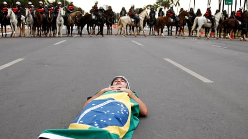 Un manifestant se couche, enveloppé dans un drapeau brésilien, en travers de la route près du stade national Mane Garrincha, à Brasilia.