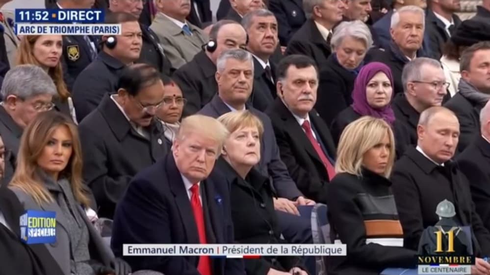 Le président du Kosovo, coupe de cheveux en brosse, cheveux gris, au deuxième rang derrière Brigitte Macron et Vladimir Poutine.