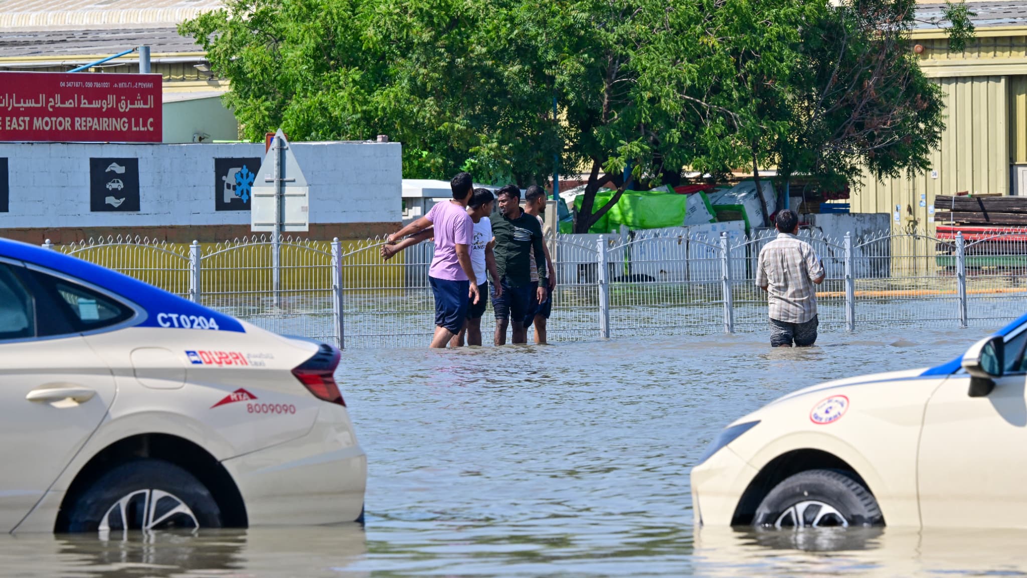 Des personnes se tiennent près de voitures bloquées dans une rue inondée de Dubaï à la suite de fortes pluies, le 18 avril 2024.
