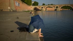 Un homme s'abrite du soleil sous un parapluie au bord de la Garonne, à Toulouse, le 20 juin 2025. 