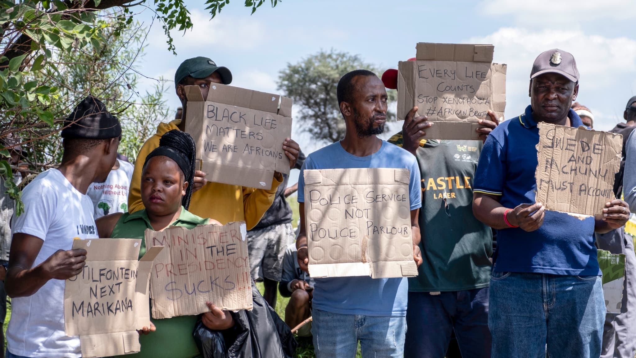 Les membres de la communauté et les travailleurs tiennent des banderoles alors qu'ils se rassemblent pour protester pendant l'opération de sauvetage visant à récupérer les mineurs illégaux d'une mine d'or abandonnée à Stilfontein, le 14 janvier 2025.