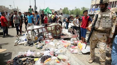 Un membre des forces de sécurité irakiennes monte la garde, alors que les civils regardent les dégâts causés par l'attaque de Daesh, dans un marché de Bagdad, le 11 mai 2016.