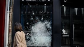 Une femme passe devant la vitrine d'un magasin un magasin endommagé après des émeutes, le 27 juin 2023 à Paris