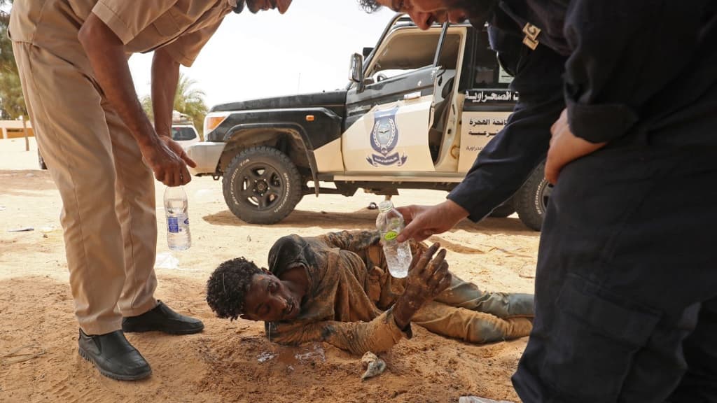 Des gardes-frontières libyens fournissent de l'eau à des migrants, près d'Al-Assah, à la frontière entre la Libye et la Tunisie, le 30 juillet 2023.