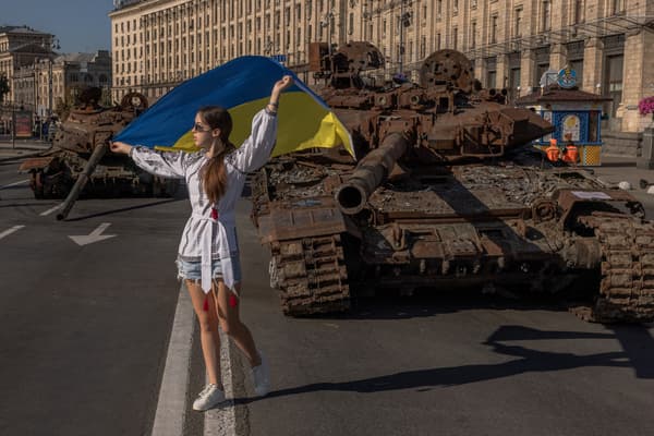 Une jeune femme pose avec un drapeau ukrainien devant des carcasses de chars russes, pour le Jour de l'Indépendance de l'Ukraine, à Kiev, le 24 août 2023