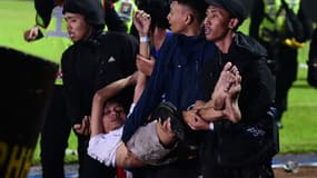 Un groupe de personnes porte un homme après un match de football entre Arema FC et Persebaya Surabaya au stade Kanjuruhan de Malang, dans l'est de Java. Au moins 127 personnes sont mortes dans un stade de football en Indonésie, le 1er octobre, lorsque des supporters ont envahi le terrain et que la police a répondu par des gaz lacrymogènes, déclenchant une bousculade, selon des responsables.