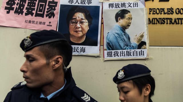 Des policiers passent devant les avis de recherche concernant Gui Minhai (à gauche), un des cinq libraires travaillant pour la maison d'édition Mighty Current, et disparus depuis 2015.