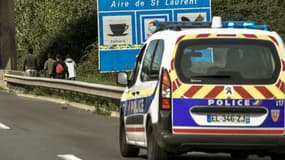 Un véhicule de police suit des migrants qui longent à pied l'autoroute A25