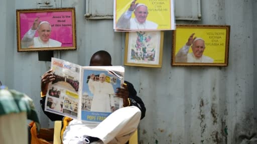 Un homme lit le journal "Catholic Mirror" devant des images du pape François à la basilique de la Sainte famille de Nairobi le 22 novembre 2015