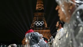 Des spectateurs protégés de la pluie par des ponchos assistent à la cérémonie d'ouverture des Jeux olympiques de Paris avec la tour Eiffel au fond, le 26 juillet 2024