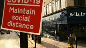 Un homme portant un masque de protection se tient à un carrefour à Liverpool (Angleterre) près d'un panneau avertissant les piétons de "maintenir la distanciation spciale", une des mesures barrière contre le Covid-19, le 2 octobre 2020