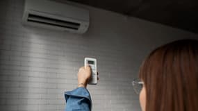 Une jeune femme règle sa climatisation avec une télécommande (photo d'illustration).
