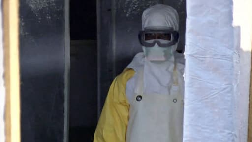 Un homme porte un masque et une combinaison de protection à l'entrée d'une tente médicale à Gueckedou, en Guinée.