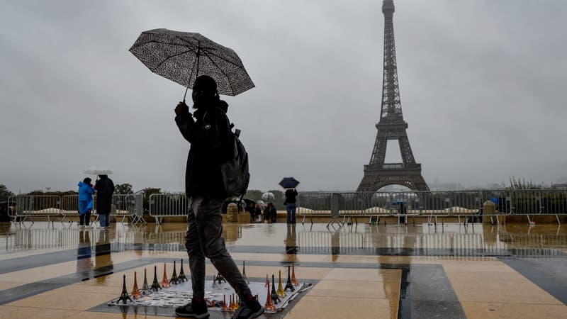 Un vendeur ambulant s'abrite de la pluie avec un parapluie sur l'esplanade du Tocadero en face de la Tour Eiffel, le 9 octobre 2024.