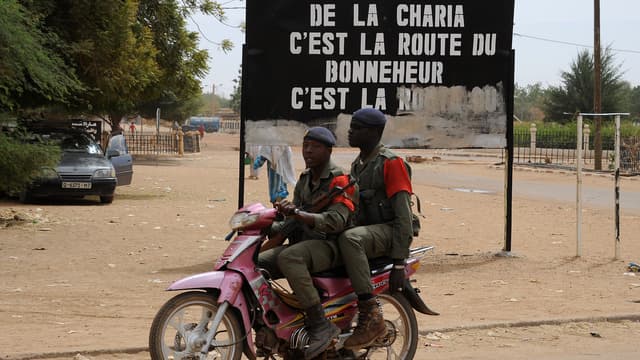 Soldats maliens circulant devant un panneau exaltant la Charia, en 2013.