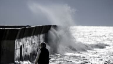 Un promeneur devant une vague qui se fracasse sur une jetée - Image d'illustration 