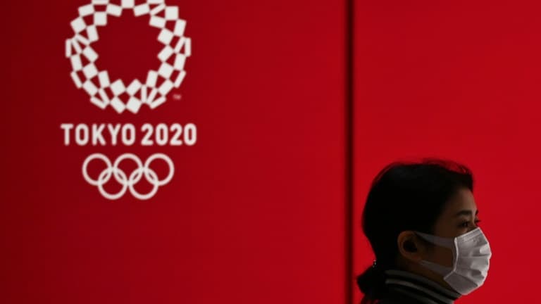 Une femme avec un masque passe devant le logo des JO de Tokyo de 2020 le 24 mars 2020 dans la capitale nippone.
