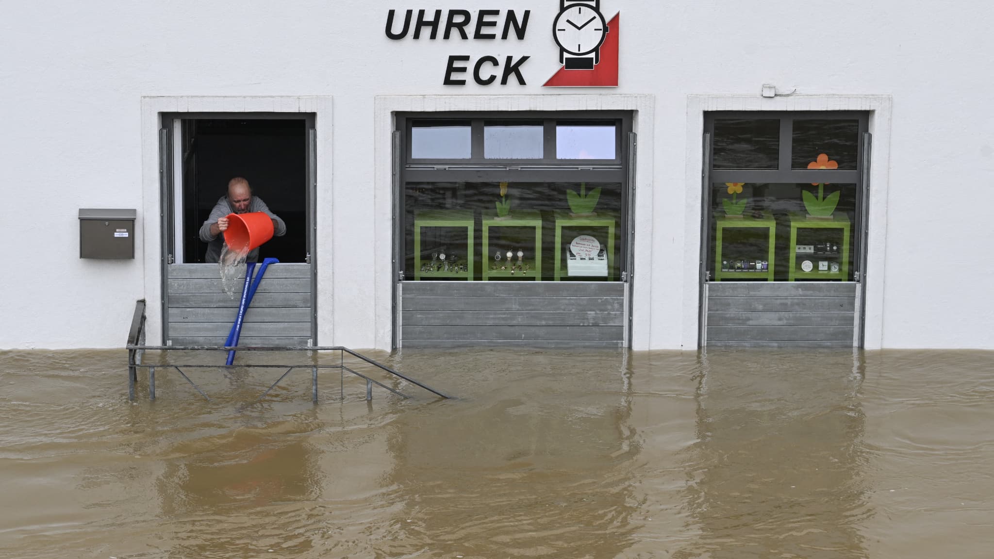 Un homme tente de déverser de l'eau avec un seau hors de son magasin de montres dans une rue et des maisons inondées dans le centre de Passau en Bavière, dans le sud de l'Allemagne, le 4 juin 2024.
