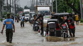 Des habitants et des automobilistes circulent sur une route inondée après le passage du super typhon Noru à San Ildefonso, dans la province de Bulacan, le 26 septembre 2022.
