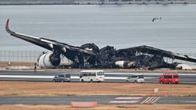 Des officiels regardent l'épave brûlée d'un avion de Japan Airlines sur le tarmac de l'aéroport international de Tokyo à Haneda à Tokyo le 3 janvier 2024, le matin après que l'avion ait percuté un plus petit avion des garde-côtes, faisant cinq morts.