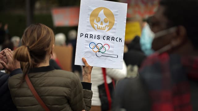 Une manifestante tient une pancarte montrant une caricature du futur logo des Jeux olympiques de Paris 2024, alors qu'elle participe à une manifestation contre l'insécurité liée au crack à Paris, le 2 octobre 2021.