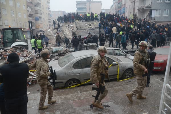 Des soldats marchent pendant que des personnes cherchent des survivants dans les décombres à Diyarbakir, le 6 février 2023, après qu'un tremblement de terre de magnitude 7.8 ait frappé le sud-est du pays.