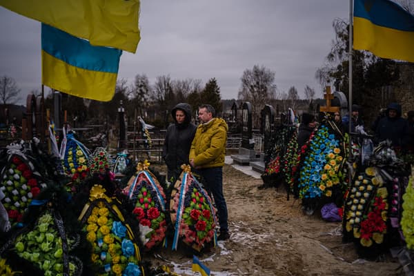 Des Ukrainiens se recueillent devant les tombes de leurs proches devant l'église Saint-André à Boutcha, un an après le début de l'offensive russe, le 24 février 2023