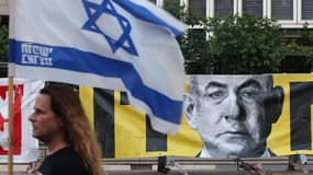 Un manifestant portant le drapeau israélien passe devant un portrait du Premier ministre Benjamin Netanyahu lors d'une manifestation anti-gouvernementale à Tel Aviv, le 7 juin 2025. 