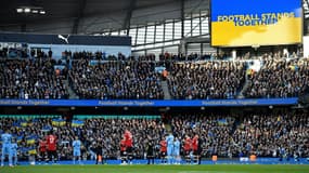 Les joueurs de Manchester City et de Manchester United participent à une minute d'applaudissements à l'unisson avec les spectateurs, en soutien de l'Ukraine, suite à l'invasion russe, avant leur derby de la 28e journée de Premier League, le 6 mars 2022 à l'Etihad Stadium