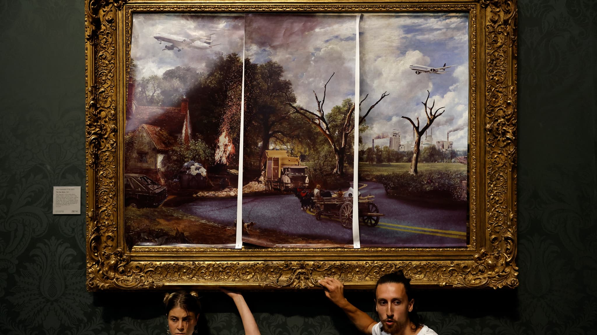 Des militants du groupe "Just Stop Oil", les mains collées au cadre du tableau "The Hay Wain" de John Constable, mais recouvert d'une version  comprenant des routes et des avions, protestent contre l'utilisation des combustibles fossiles, à la National Gallery de Londres, le 4 juillet 2022.