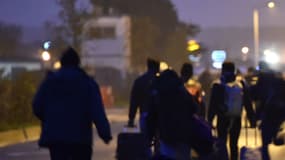 Des migrants passent avec leurs bagages devant un panneau "Calais, le 24 octobre 2016. 