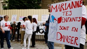 Des manifestants tiennent des pancartes lors d’un rassemblement d’anciens enfants placés, en hommage aux enfants placés morts alors qu’ils étaient à l’Aide sociale à l’enfance (ASE), sur la place Jacques Bainville près de l’Assemblée nationale à Paris, le 7 mai 2024.