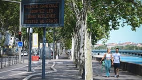 Des piétons à prpximité d'un panneau municipal alertant de la canicule en cours, le 18 août 2023 à Lyon