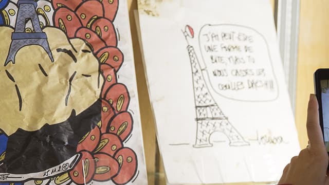 Une personne prend en photo des dessins en hommage au 13-Novembre, exposés aux Archives de Paris