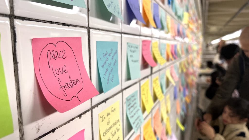 Des passagers du métro de New York apposent des Post-it sur le mur d'une station, novembre 2024