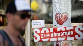 Un homme passe devant une vitrine où une affichette indique que le magasin est climatisé, pendant les soldes, le 13 juillet 2022 à Nantes